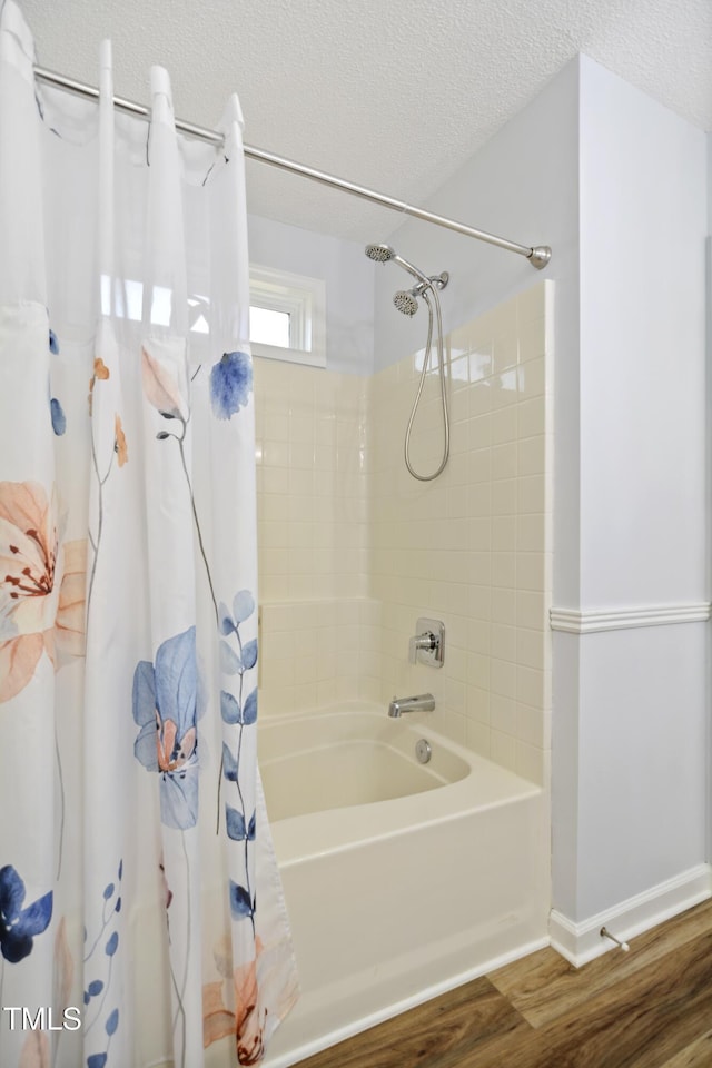 bathroom with wood finished floors, a textured ceiling, shower / bathtub combination with curtain, and baseboards