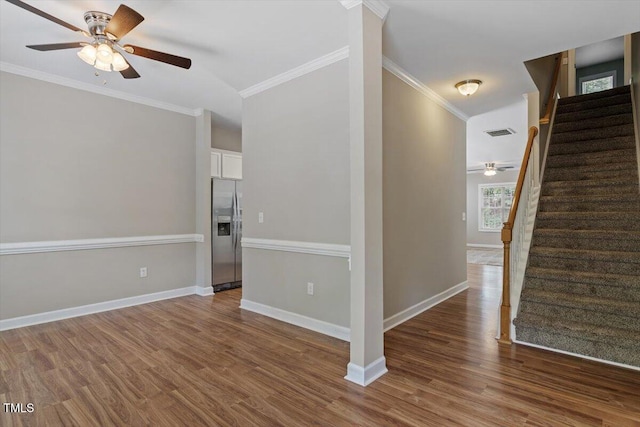 empty room featuring a ceiling fan, stairway, dark wood-style flooring, crown molding, and baseboards