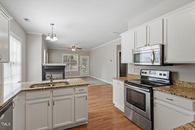 kitchen featuring stainless steel appliances, a sink, light wood-style floors, a multi sided fireplace, and white cabinetry