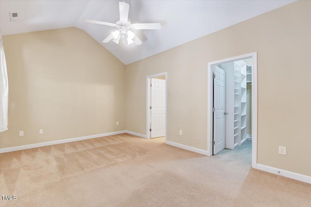 unfurnished bedroom with light carpet, lofted ceiling, a walk in closet, and baseboards