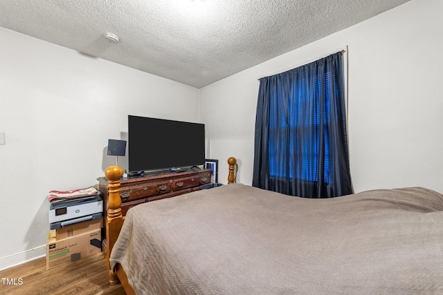 bedroom with wood finished floors, a textured ceiling, and baseboards