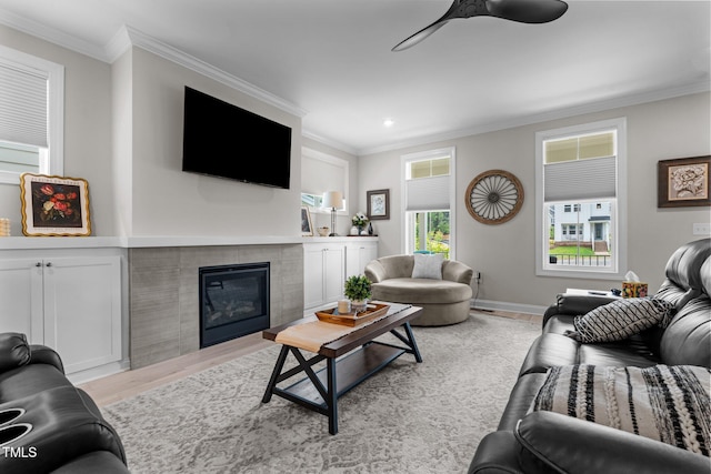 living area with wood finished floors, a ceiling fan, a tile fireplace, crown molding, and baseboards