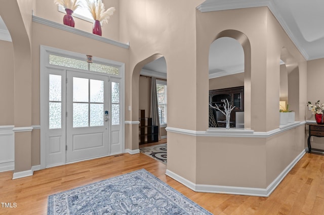 entrance foyer featuring arched walkways, wood finished floors, baseboards, and ornamental molding