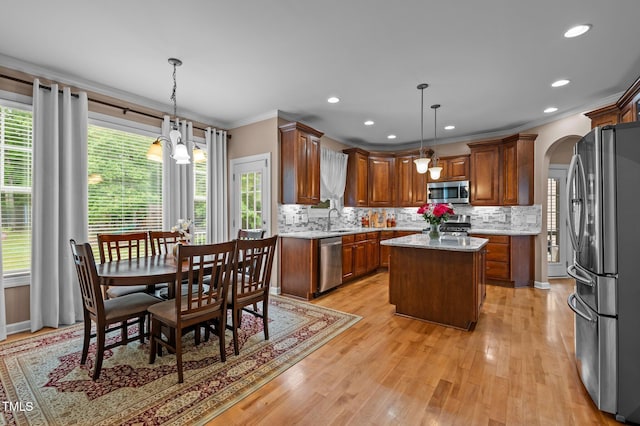 kitchen featuring appliances with stainless steel finishes, ornamental molding, arched walkways, a sink, and a center island