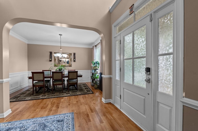 dining space with arched walkways, light wood finished floors, ornamental molding, a wainscoted wall, and a chandelier