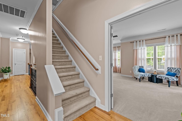 stairway with baseboards, wood finished floors, and crown molding