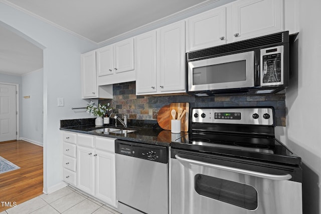 kitchen featuring appliances with stainless steel finishes, a sink, crown molding, backsplash, and white cabinetry