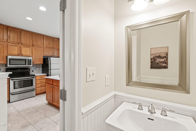 bathroom with a sink, wainscoting, tasteful backsplash, tile patterned flooring, and recessed lighting