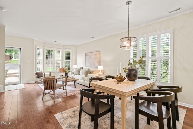 dining room with hardwood / wood-style floors, crown molding, a chandelier, and baseboards