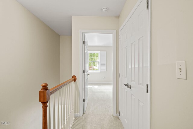 corridor with an upstairs landing, light colored carpet, and baseboards