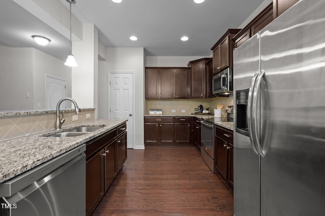 kitchen with appliances with stainless steel finishes, a sink, dark wood-type flooring, light stone counters, and backsplash
