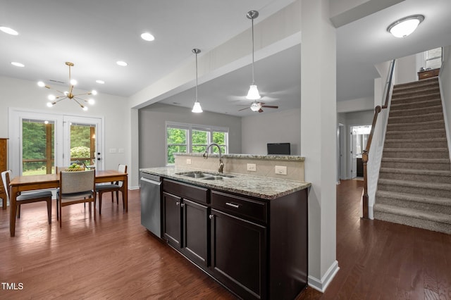 kitchen with a sink, stainless steel dishwasher, light stone countertops, dark wood finished floors, and pendant lighting