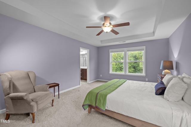 bedroom with light colored carpet, baseboards, a raised ceiling, a ceiling fan, and connected bathroom