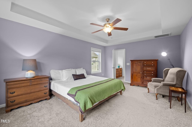 bedroom featuring light carpet, a tray ceiling, baseboards, and ceiling fan