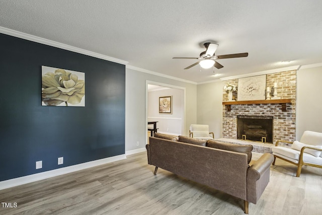 living room with light wood-style flooring, ceiling fan, a fireplace, baseboards, and ornamental molding
