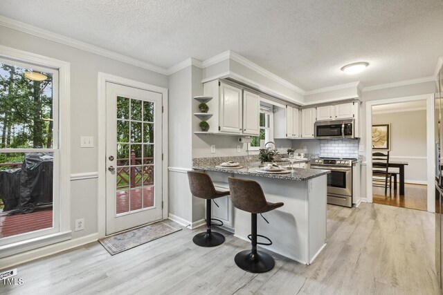 kitchen with stainless steel appliances, a peninsula, open shelves, light wood-style flooring, and a textured ceiling
