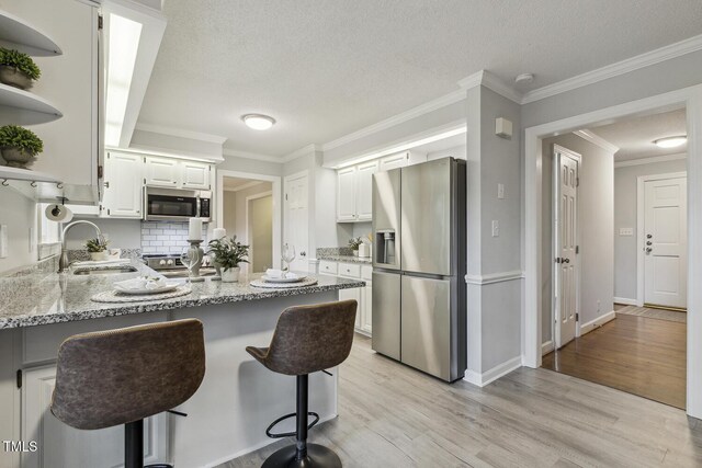 kitchen with appliances with stainless steel finishes, a sink, open shelves, a peninsula, and light wood-style floors