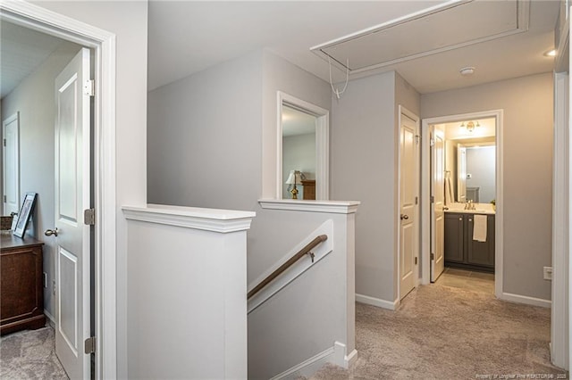 corridor featuring attic access, an upstairs landing, light carpet, baseboards, and a sink