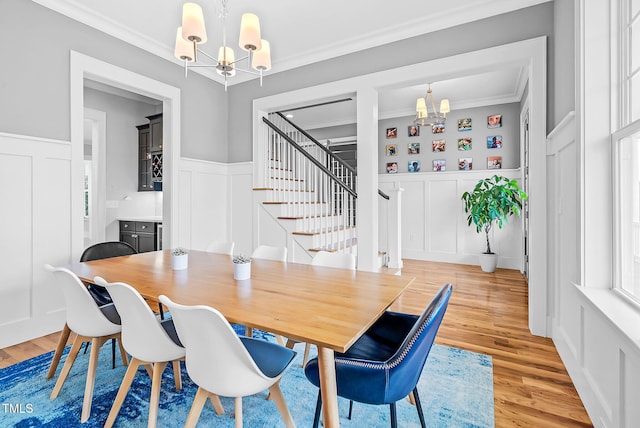 dining room with a chandelier, a decorative wall, ornamental molding, light wood-style flooring, and a wainscoted wall