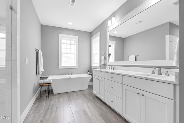 full bathroom featuring baseboards, double vanity, a freestanding tub, tiled shower, and recessed lighting