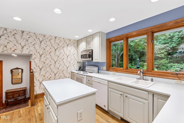 kitchen with wallpapered walls, white appliances, a sink, light countertops, and an accent wall