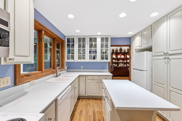 kitchen with white appliances, a sink, light wood finished floors, glass insert cabinets, and recessed lighting