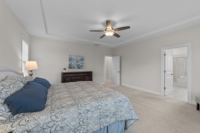 carpeted bedroom with a tray ceiling, baseboards, ensuite bathroom, and a ceiling fan