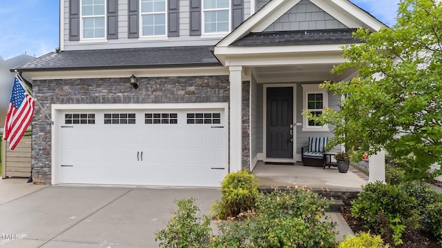 entrance to property with stone siding, driveway, a garage, and covered porch