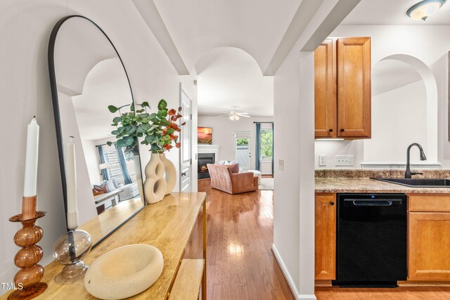 2635 Asher View Ct, Raleigh, NC 27606 - kitchen with black dishwasher, a sink, a warm lit fireplace, ceiling fan, and light wood-style floors