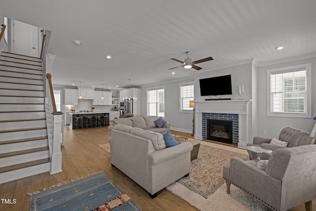 living room featuring ceiling fan, stairs, a fireplace with flush hearth, recessed lighting, and crown molding