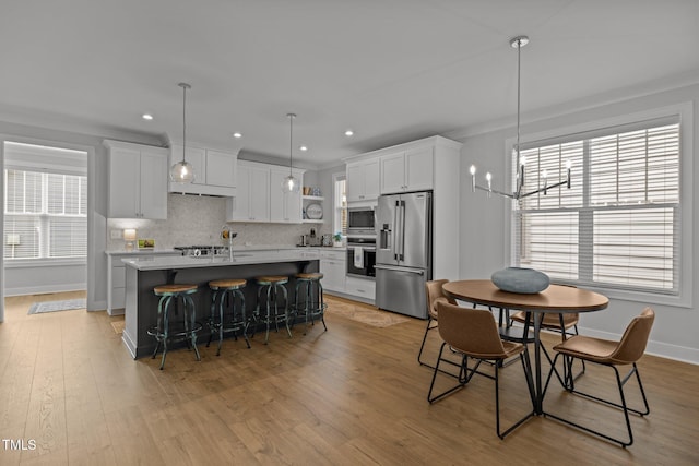kitchen featuring stainless steel appliances, a center island with sink, light wood finished floors, decorative backsplash, and white cabinets