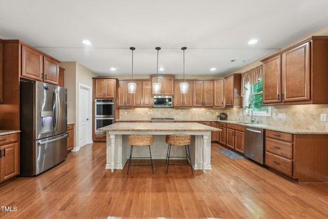 kitchen featuring appliances with stainless steel finishes, a sink, brown cabinetry, a breakfast bar area, and a kitchen island