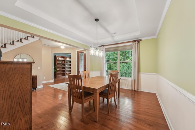 dining area with a tray ceiling, wood finished floors, ornamental molding, and stairs