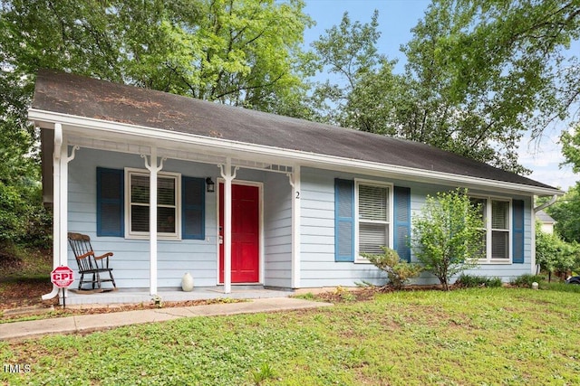 ranch-style home with a porch, a front yard, and roof with shingles