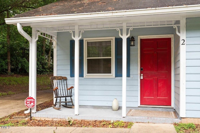 property entrance featuring covered porch and a shingled roof