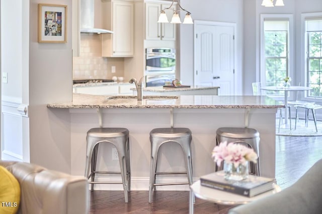 2916 Reynolda Cir, Durham, NC 27712 - kitchen with wall chimney exhaust hood, a sink, a breakfast bar, dark wood-type flooring, and tasteful backsplash