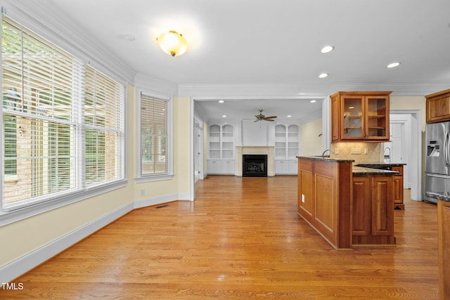 1010 Mill Pointe Way, Elon, NC 27244 - kitchen with stainless steel fridge, a ceiling fan, a fireplace, glass insert cabinets, and brown cabinetry