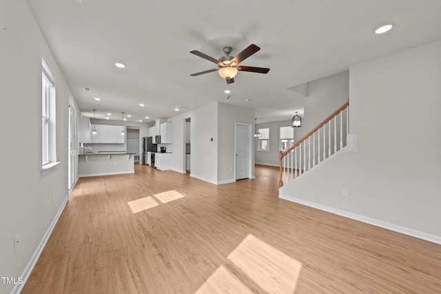 unfurnished living room featuring light wood-style flooring, recessed lighting, ceiling fan, baseboards, and stairs
