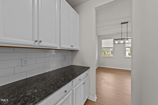 kitchen with decorative backsplash, white cabinets, dark stone counters, and baseboards