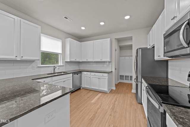 kitchen featuring appliances with stainless steel finishes, a sink, white cabinetry, dark stone countertops, and light wood-style floors