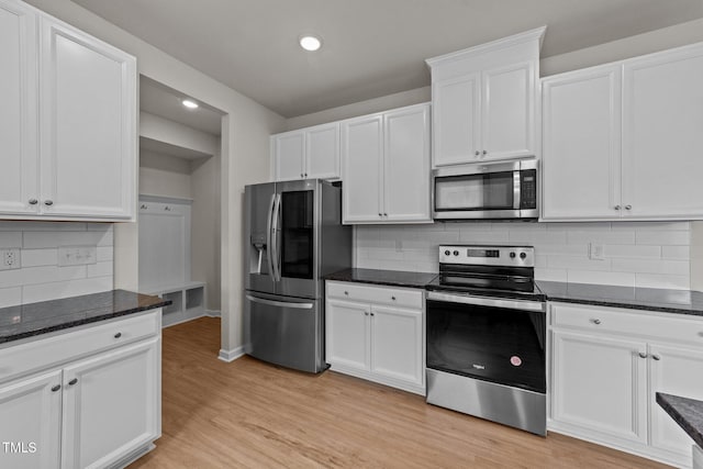 kitchen featuring appliances with stainless steel finishes, white cabinetry, light wood-type flooring, tasteful backsplash, and dark stone counters
