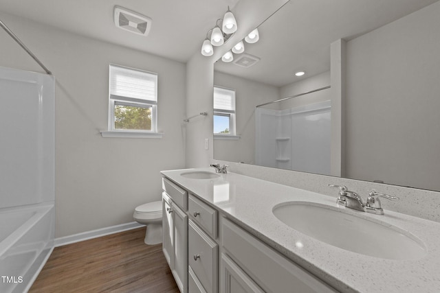 bathroom with toilet, baseboards, wood finished floors, double vanity, and tub / shower combination