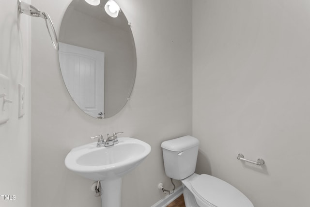 half bathroom with toilet, wood finished floors, and a sink