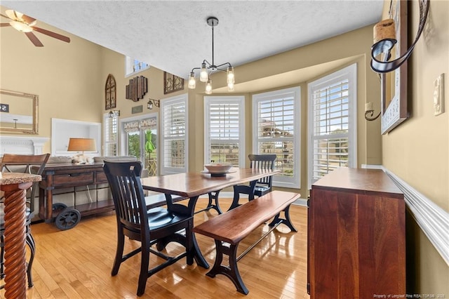 dining space featuring a textured ceiling, light wood-style floors, plenty of natural light, a chandelier, and a ceiling fan
