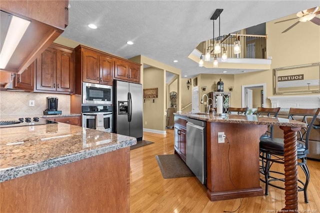 kitchen featuring stainless steel appliances, light stone countertops, light wood-style floors, a kitchen breakfast bar, and baseboards