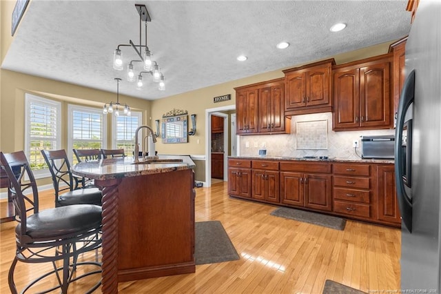 kitchen featuring a sink, freestanding refrigerator, light wood-style flooring, a kitchen bar, and a textured ceiling