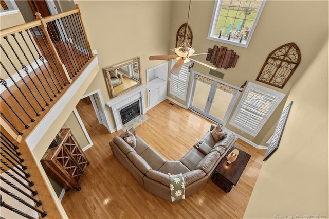 living area featuring a towering ceiling, wood finished floors, ceiling fan, baseboards, and a premium fireplace
