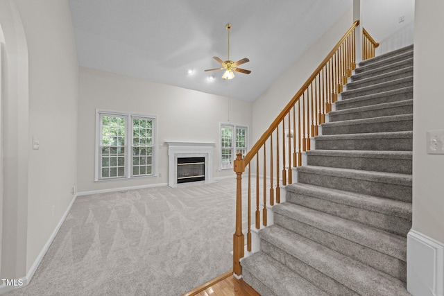 stairway featuring a high end fireplace, a ceiling fan, baseboards, carpet floors, and vaulted ceiling