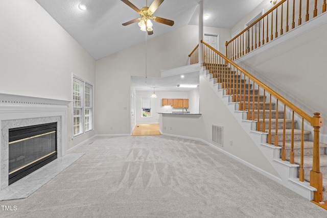 unfurnished living room featuring ceiling fan, high vaulted ceiling, carpet, a high end fireplace, and stairs