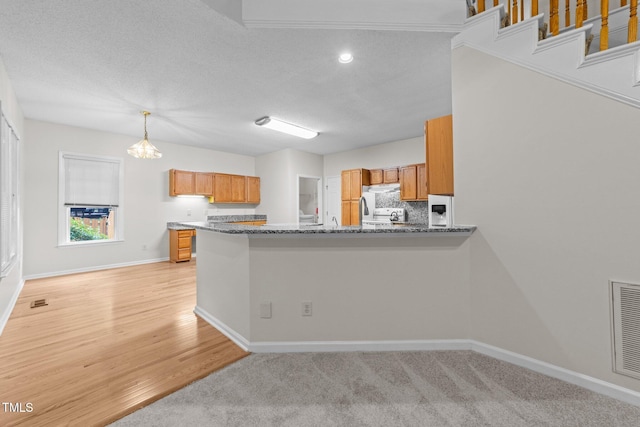 kitchen featuring refrigerator, brown cabinets, baseboards, a peninsula, and stone countertops